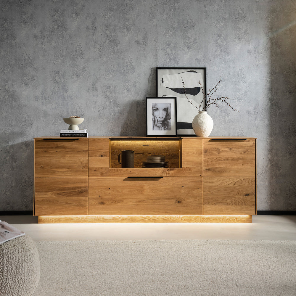 Sideboard aus massiver Wildeiche mit schwarzen Griffen und integrierter Beleuchtung vor graue Wand in Betn-Optik