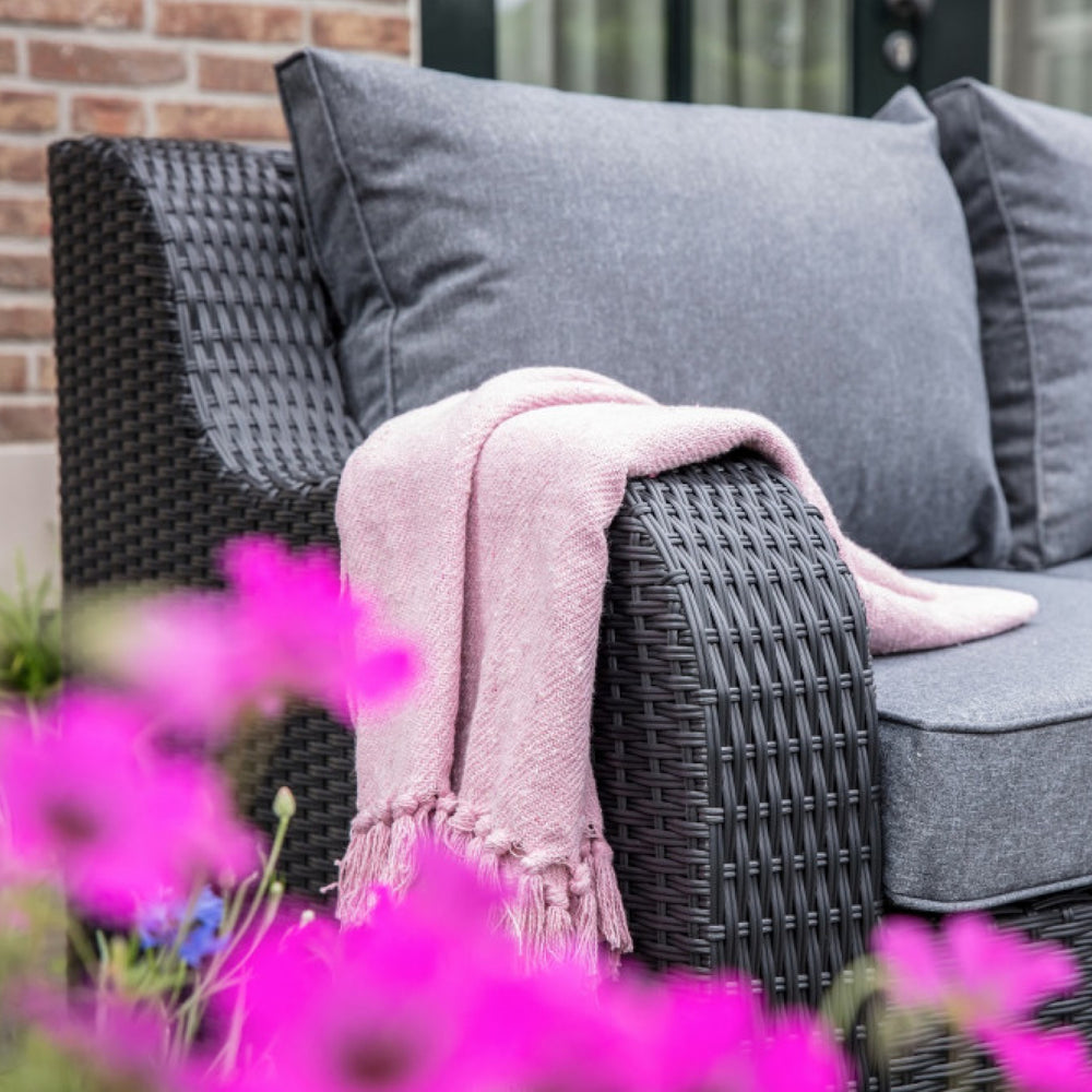dunkelgraue Gartenmöbel mit bequemen Kissen und rosafarbener Decke; pinke Blumen im Vordergrund